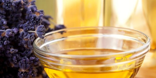Glass bowl with golden oil and dried lavender on a wooden surface.
