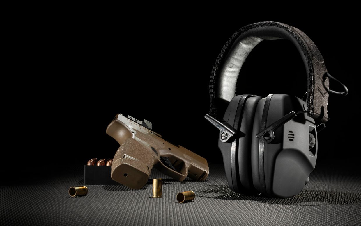 A pistol, bullets, and protective earmuffs on a textured surface.