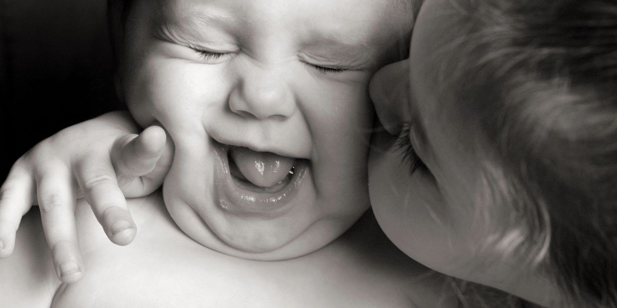 Baby laughing while kissed by another child.