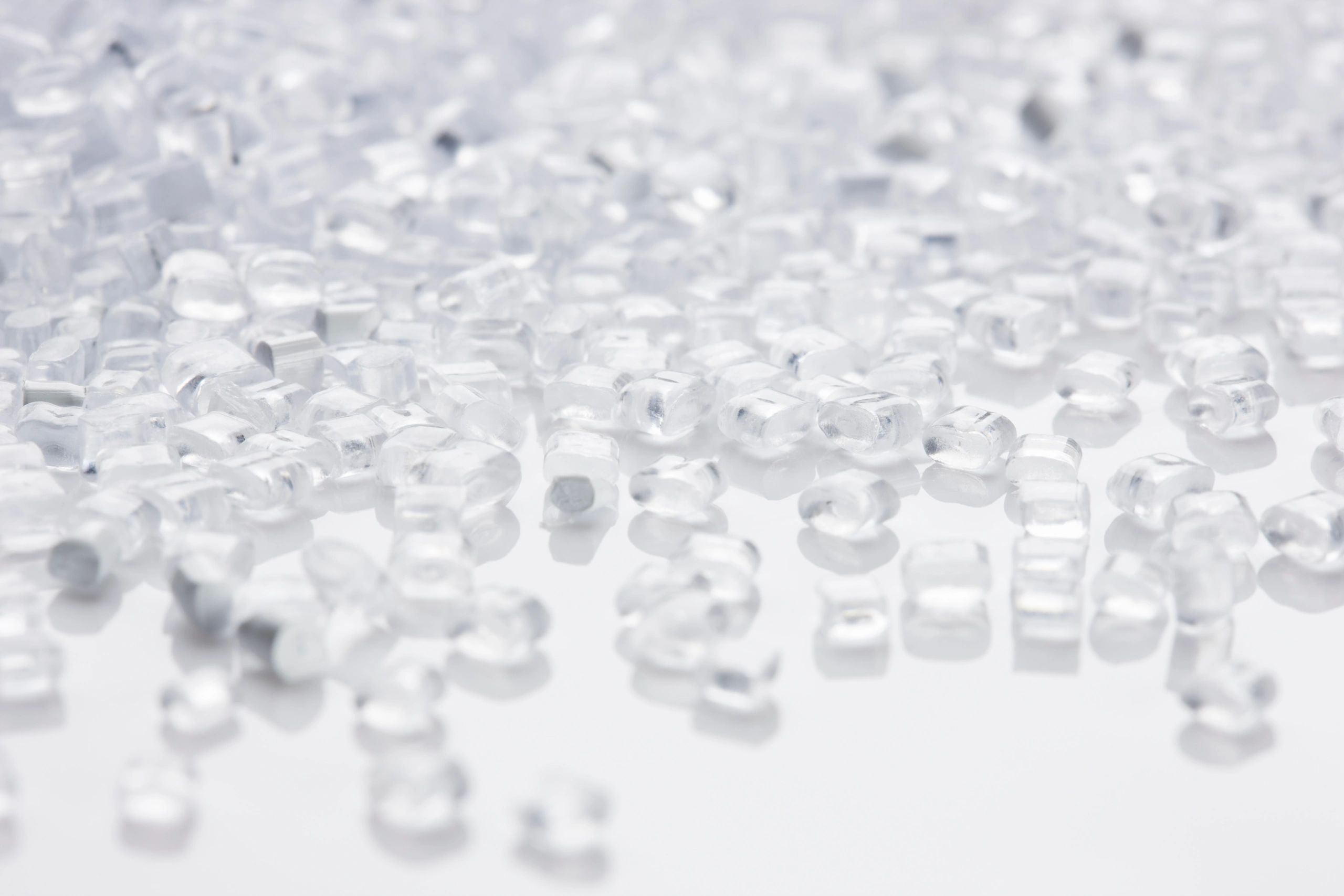 Close-up of clear plastic pellets scattered on a white surface.