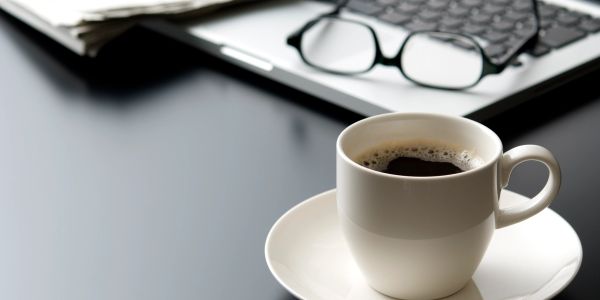 A cup of coffee on a desk with glasses and a laptop.