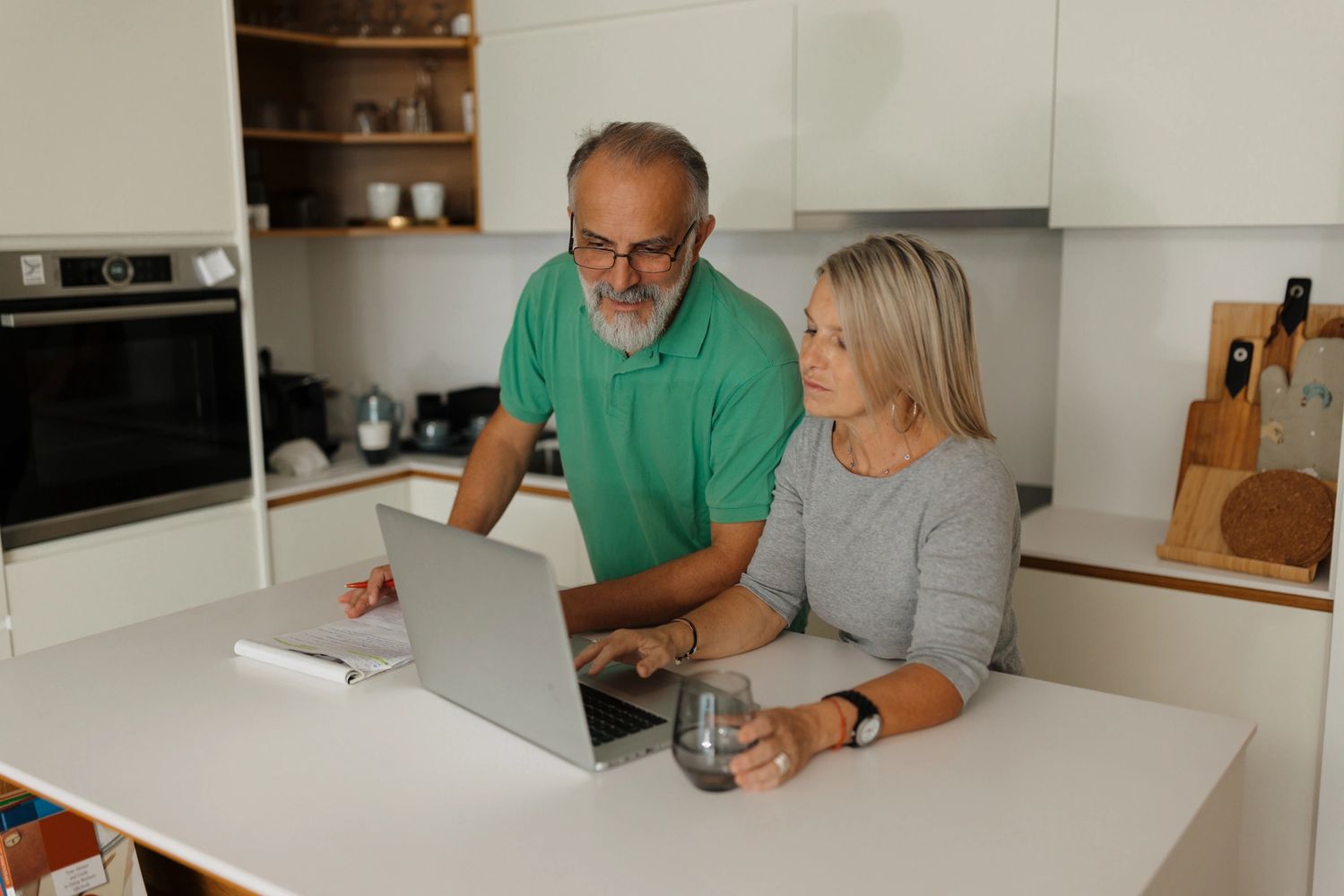 Mature couple using laptop in modern kitchen, engaged in planning or research.