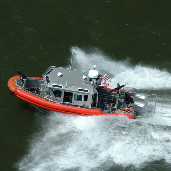 A fast-moving orange and gray patrol boat with mounted guns on water.