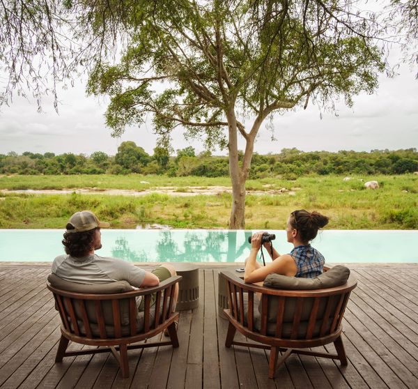 Two people relaxing by a pool with a nature view.