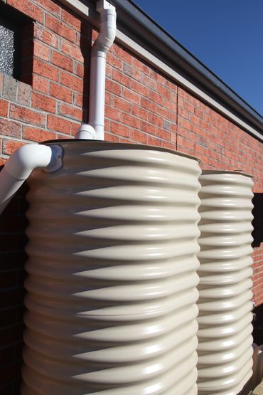 Two large beige water tanks next to a brick wall with blue sky above.