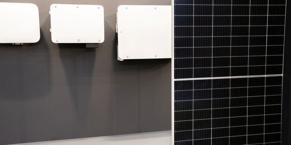 Solar panel next to three white electrical boxes on a gray wall.