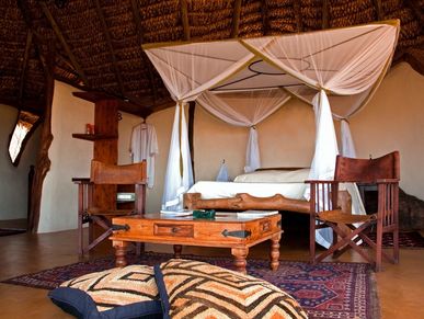 Rustic bedroom with a canopy bed and wooden furniture under a thatched roof.