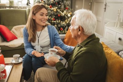 A young woman and an elderly man sharing tea near a Christmas tree.
