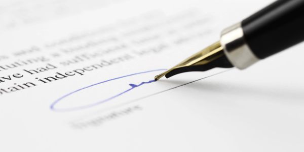 A pen signing a document with a blue signature.
