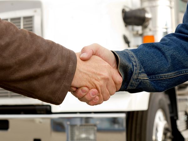 Two people shaking hands, one in a brown jacket, the other in denim.