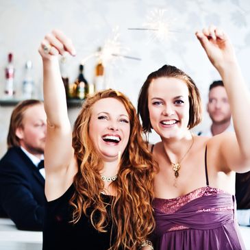 Two women joyfully holding sparklers at a party.