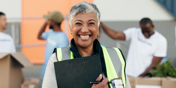 Smiling volunteer in safety vest with clipboard.