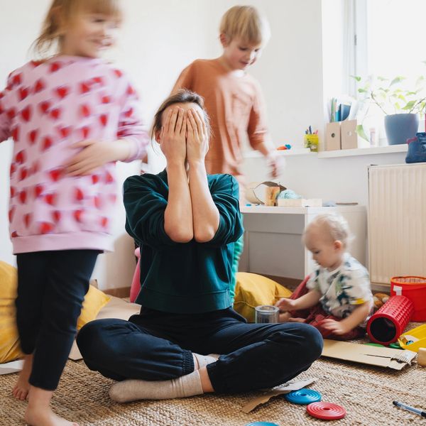 A woman playing peekaboo with three children in a bright playroom.