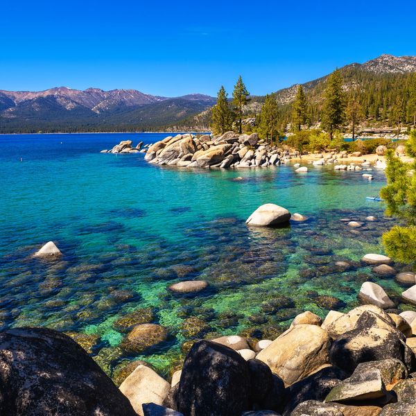 Clear turquoise lake surrounded by rocky shores and pine trees under a bright blue sky.