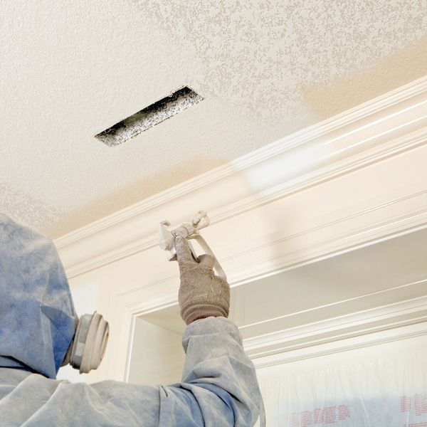 Person spray painting a ceiling corner with protective gear.