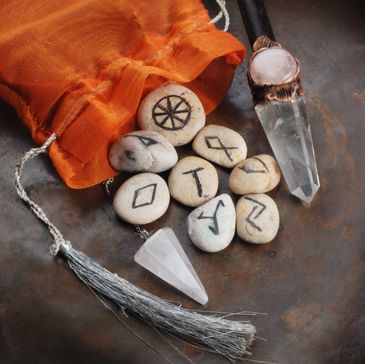 Runes on stones spilling from an orange pouch next to crystal pendulums.