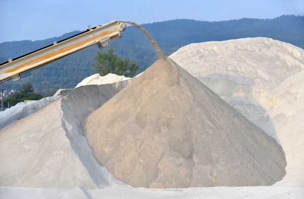 Conveyor pouring sand onto a large pile outdoors.