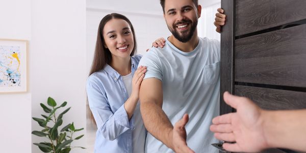 Happy couple welcoming a guest at their home with a handshake.