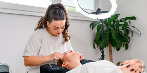 Woman applies eyelash extensions to a client.