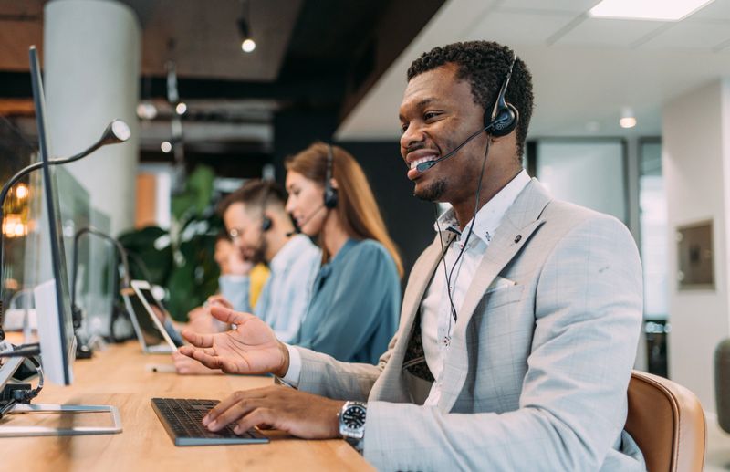 Shot of call center operators working in the office. Call center agent working with his colleagues in modern office. Smiling handsome businessman working in call center.