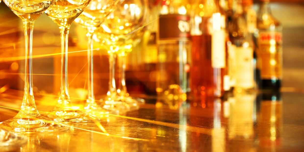 Golden light reflecting off wine glasses and bottles on a bar counter.