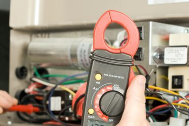Hand-held clamp meter measuring electrical current in a wiring panel.