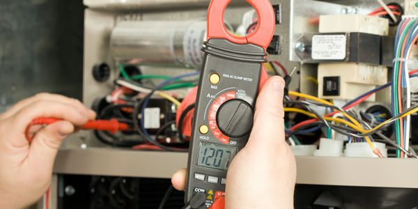 Hand-held clamp meter measuring electrical current in a wiring panel.