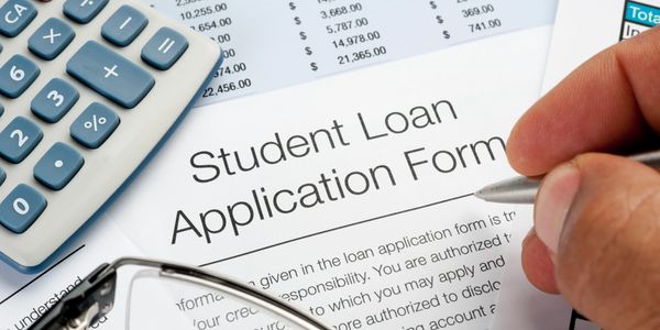 Person filling out a student loan application form with a calculator nearby.