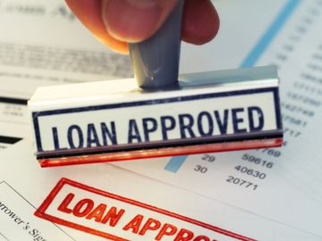 A hand stamping a document with "LOAN APPROVED" in bold letters.
