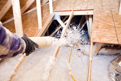 Hand spraying loose-fill insulation in an attic space.