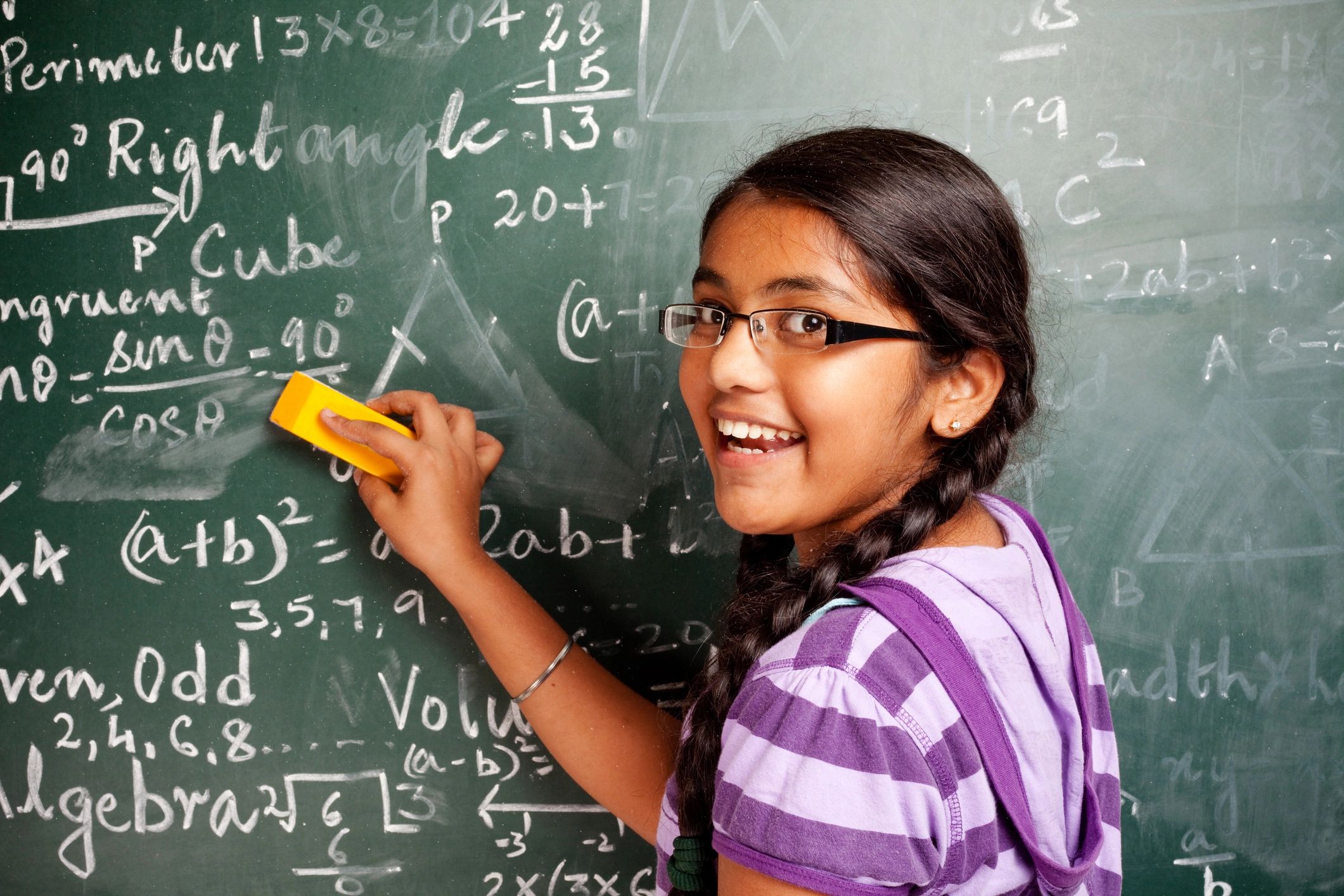 Smiling girl erasing chalkboard filled with math formulas.