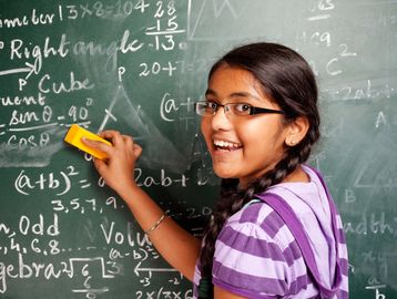 Smiling girl erasing math equations on a chalkboard.