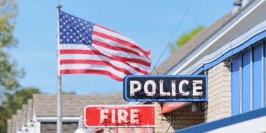 American flag waves above police and fire department signs on a sunny day.