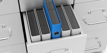 Open filing cabinet drawer with organized binders, one blue standing out.