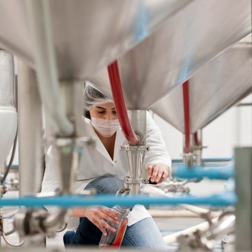 A lab technician collects liquid from industrial equipment in a clean facility.