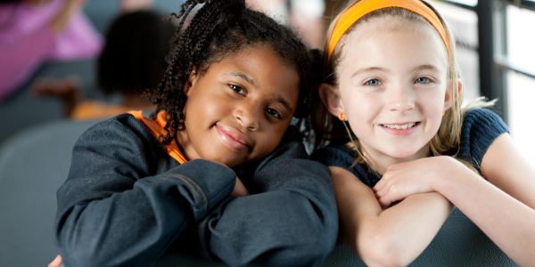 Two young girls smiling and leaning on a surface.