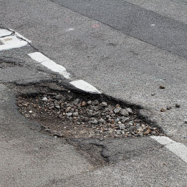 A large pothole filled with gravel on an asphalt road.