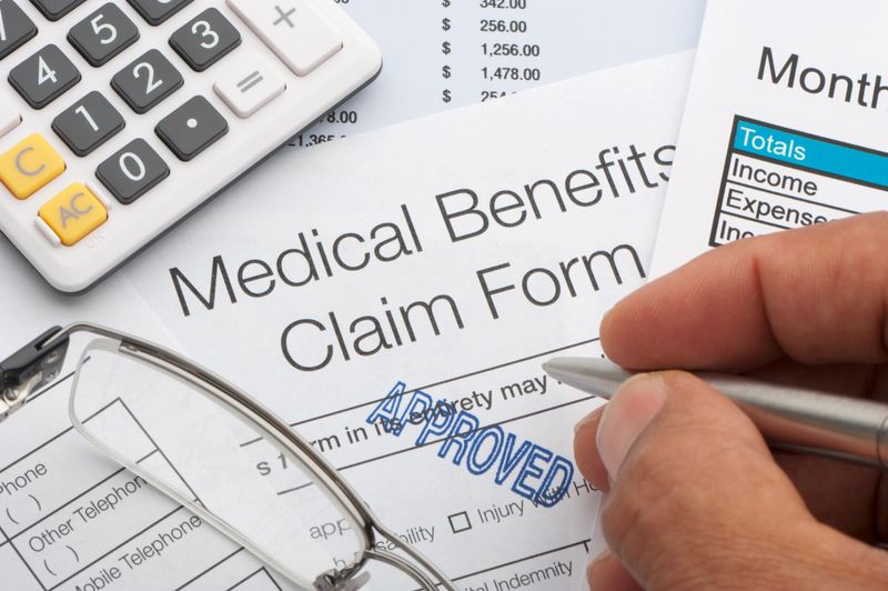 Close up approved Medical benefits claim form with calculator, pen, expenses list and writing hand