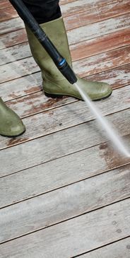 Person pressure washing a wooden deck wearing green boots.