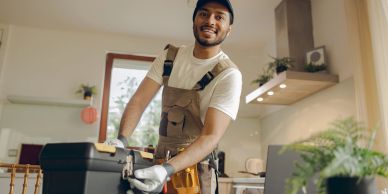 Smiling handyman holding a toolbox indoors.