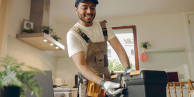 Smiling repairman opening a black toolbox in a bright kitchen.