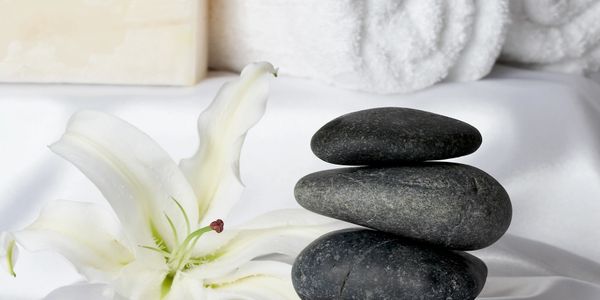 Stacked black stones with a white lily flower and rolled towels in a spa setting.