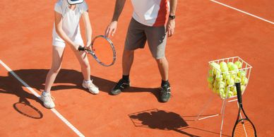 A tennis coach teaching a young player on a clay court.