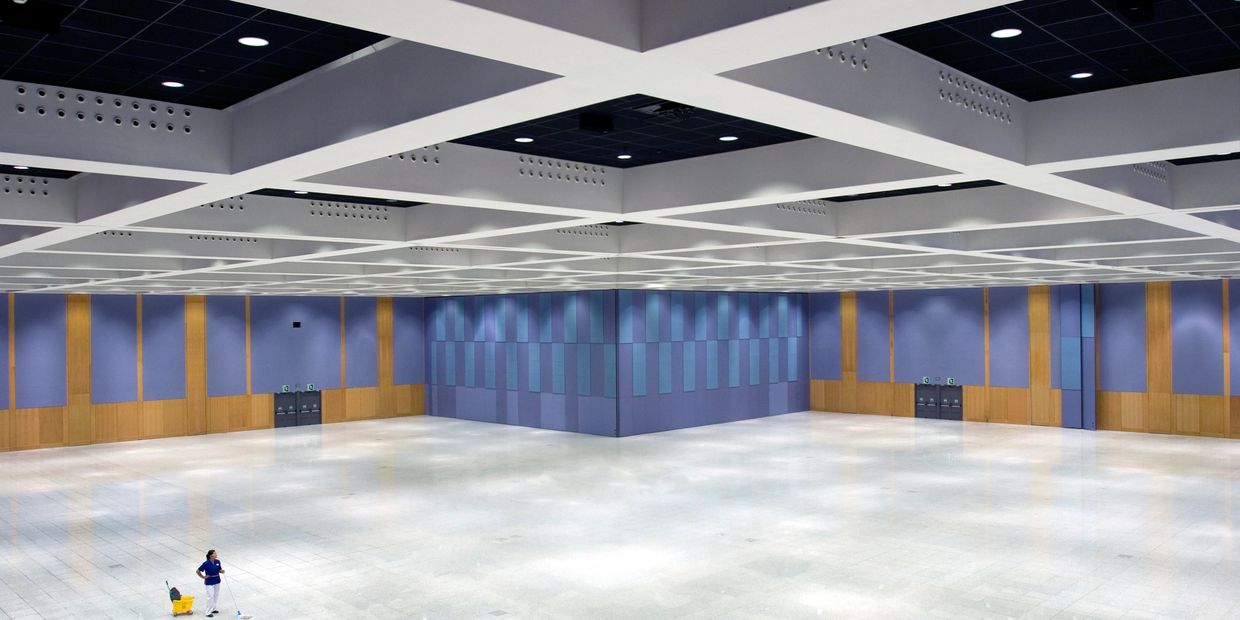 A lone cleaner mops the floor of a vast, empty hall with modern design.