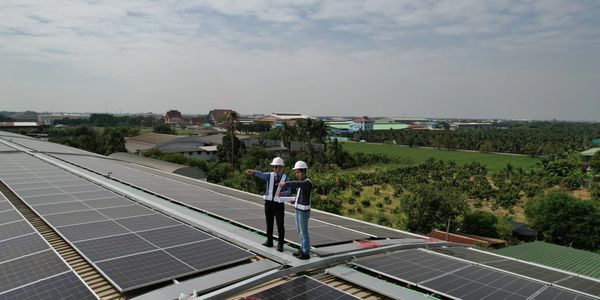Two engineers inspect solar panels on a rooftop overlooking green fields.