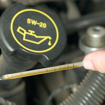 Checking engine oil level with dipstick near oil cap.