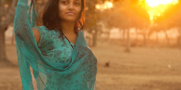 Woman in teal dress standing outdoors during golden hour.