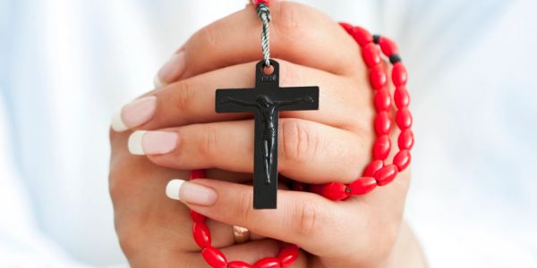 Hands holding a black crucifix with red rosary beads.