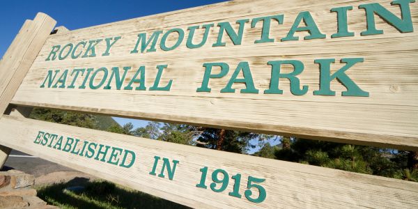 Road sign for Buffalo Bill Dam Visitor Center near a mountainous lake.