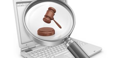 A magnifying glass focuses on a judge's gavel over a laptop keyboard.